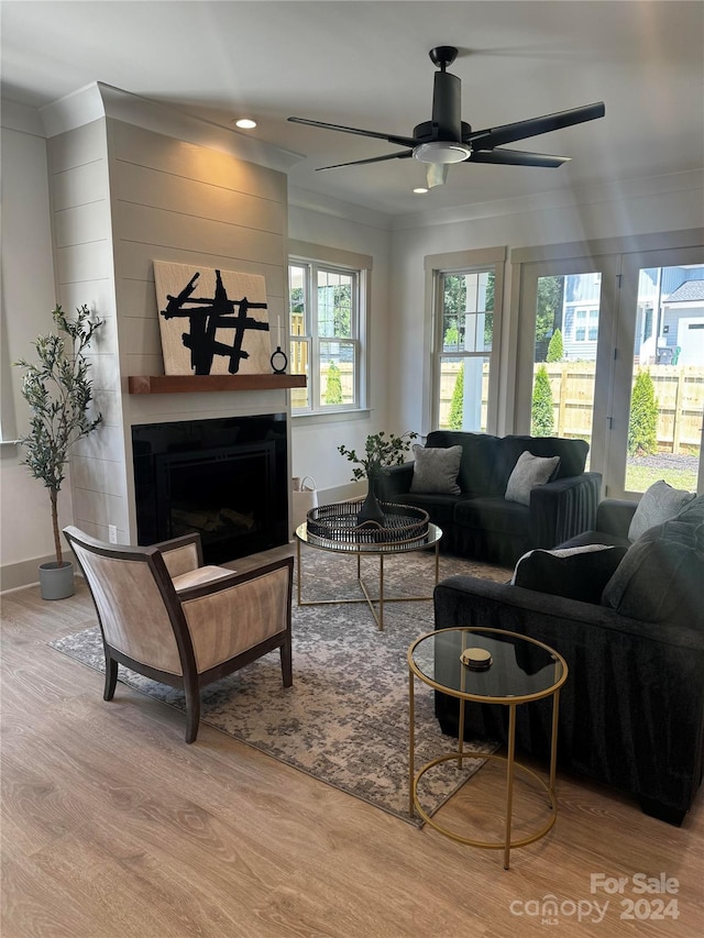 living room with a large fireplace, ceiling fan, wood finished floors, and crown molding