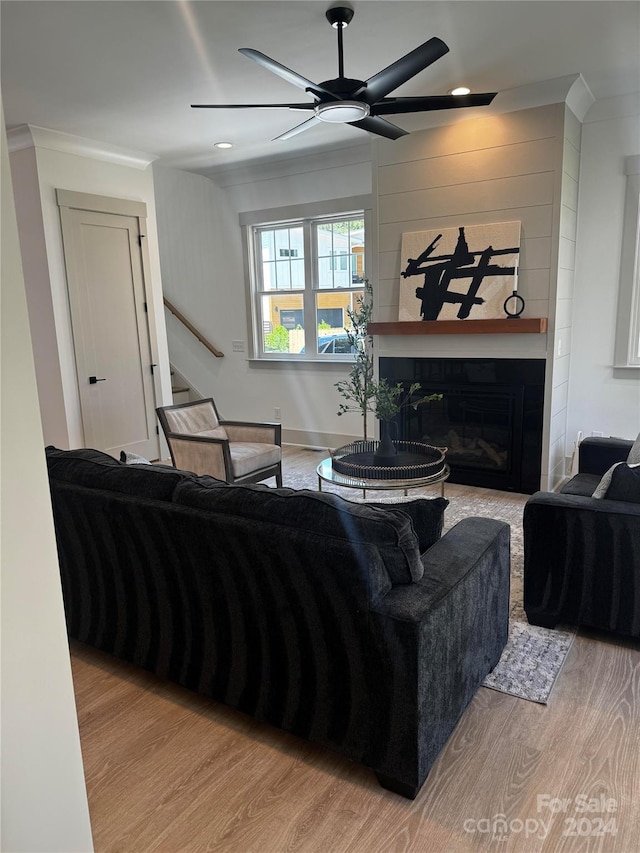 living room featuring a large fireplace, light hardwood / wood-style flooring, ceiling fan, and ornamental molding