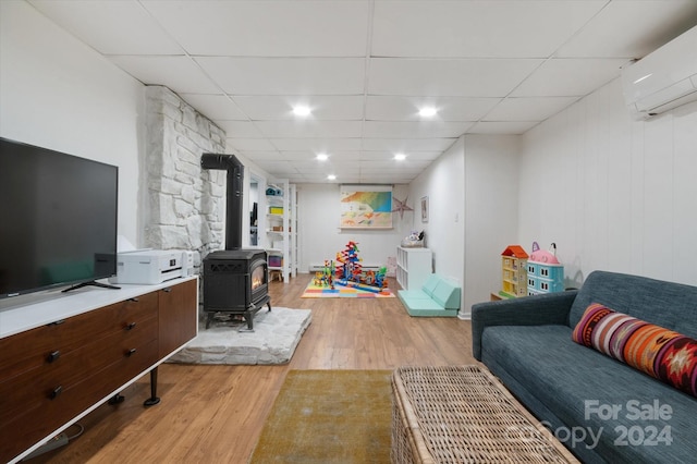 living room with a wood stove, a drop ceiling, a wall unit AC, and light hardwood / wood-style flooring