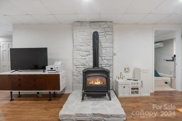 details featuring a drop ceiling, hardwood / wood-style floors, a wall unit AC, and a wood stove