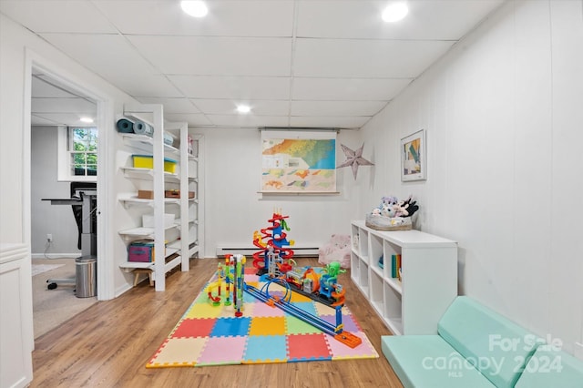 recreation room with hardwood / wood-style floors, a drop ceiling, and baseboard heating