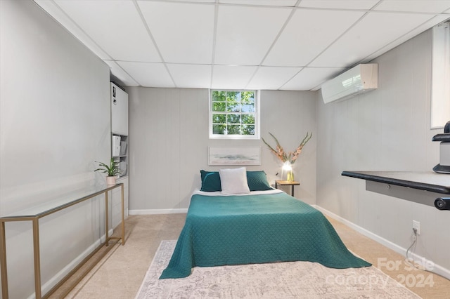 bedroom featuring a drop ceiling, a wall mounted air conditioner, and light colored carpet