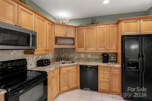 kitchen with tasteful backsplash, light stone counters, sink, black appliances, and light tile patterned floors