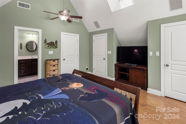 bedroom with vaulted ceiling with skylight, ceiling fan, light wood-type flooring, and connected bathroom