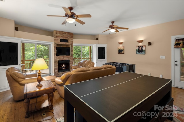 recreation room with a stone fireplace, ceiling fan, and hardwood / wood-style flooring