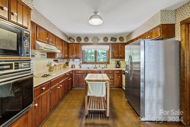 kitchen featuring sink, dark tile patterned flooring, black appliances, a textured ceiling, and a center island