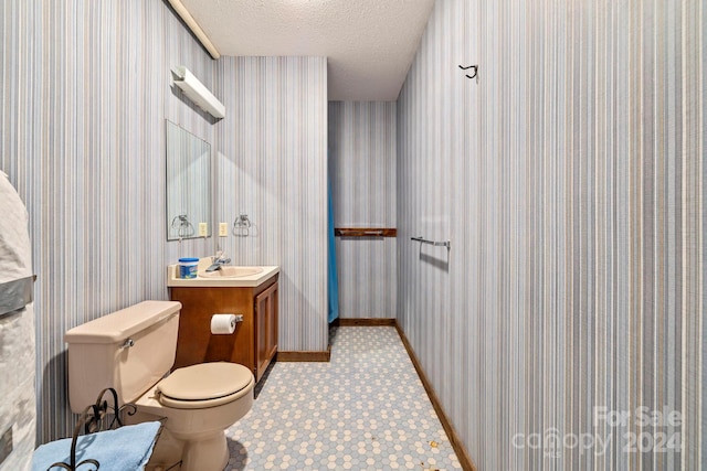 bathroom with a textured ceiling, toilet, tile patterned flooring, and vanity