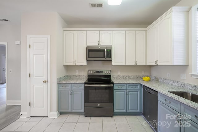 kitchen with light tile patterned floors, gray cabinetry, stainless steel appliances, light stone counters, and white cabinets