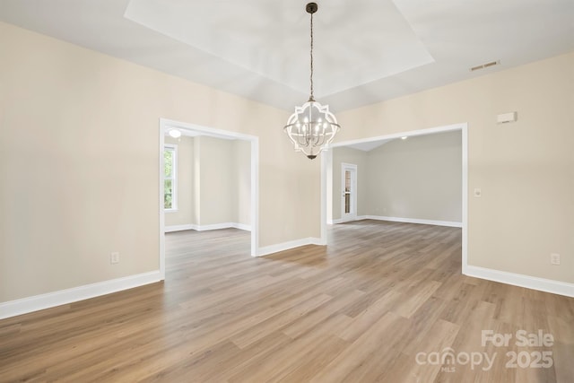 spare room with a notable chandelier, a tray ceiling, and light wood-type flooring