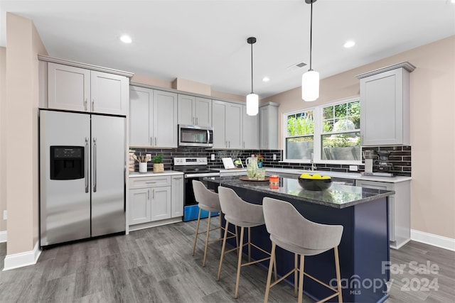 kitchen with hanging light fixtures, decorative backsplash, hardwood / wood-style floors, a center island, and appliances with stainless steel finishes