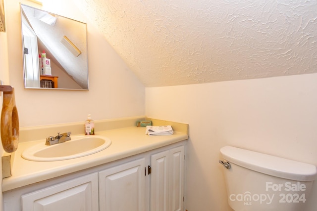 bathroom featuring a textured ceiling, toilet, vanity, and vaulted ceiling