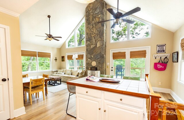 kitchen with tile countertops, light wood-type flooring, high vaulted ceiling, white cabinets, and a breakfast bar