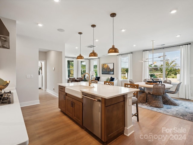 kitchen featuring pendant lighting, stainless steel dishwasher, a center island with sink, sink, and light hardwood / wood-style flooring