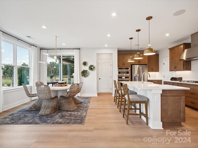 kitchen featuring light hardwood / wood-style floors, pendant lighting, sink, appliances with stainless steel finishes, and an island with sink