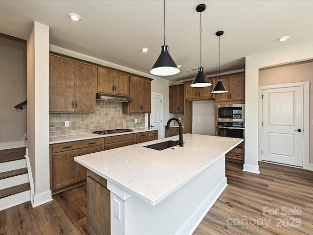 kitchen featuring dark wood-type flooring, a sink, under cabinet range hood, stainless steel appliances, and decorative backsplash