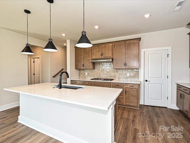 kitchen with visible vents, a sink, under cabinet range hood, gas cooktop, and decorative backsplash