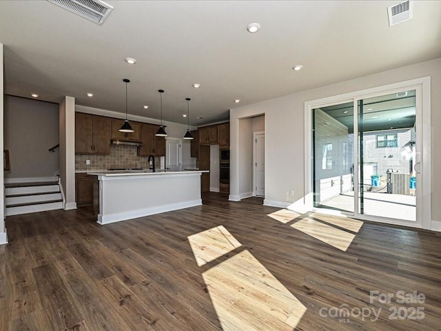 kitchen with light countertops, an island with sink, visible vents, and dark wood-type flooring
