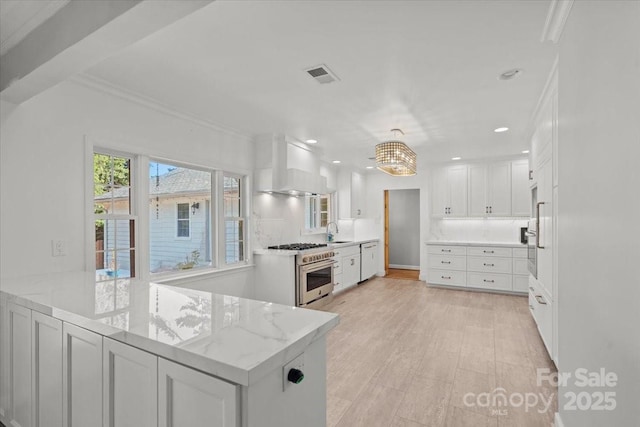 kitchen with pendant lighting, stainless steel stove, white cabinets, light stone counters, and kitchen peninsula