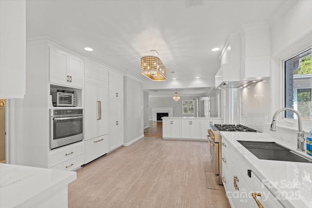 kitchen featuring pendant lighting, sink, appliances with stainless steel finishes, light stone countertops, and white cabinets