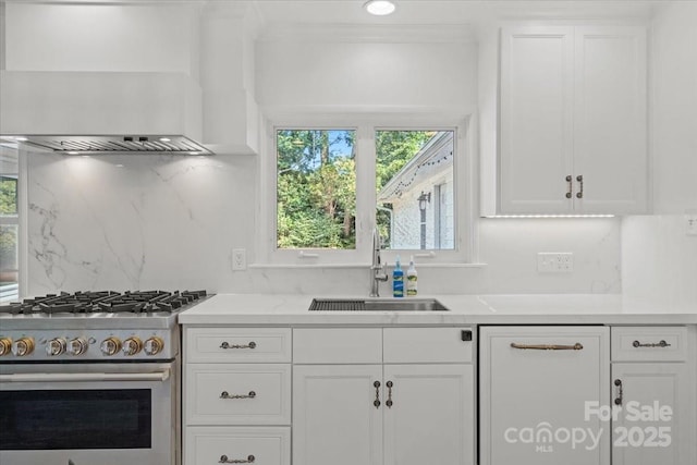 kitchen featuring sink, wall chimney range hood, high end stainless steel range oven, tasteful backsplash, and white cabinets