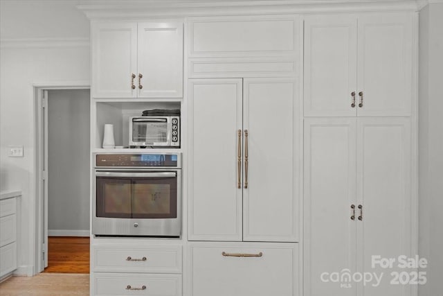 kitchen with white cabinetry, crown molding, light hardwood / wood-style flooring, and oven