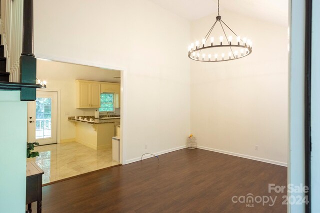 unfurnished dining area with an inviting chandelier, high vaulted ceiling, sink, and dark hardwood / wood-style floors