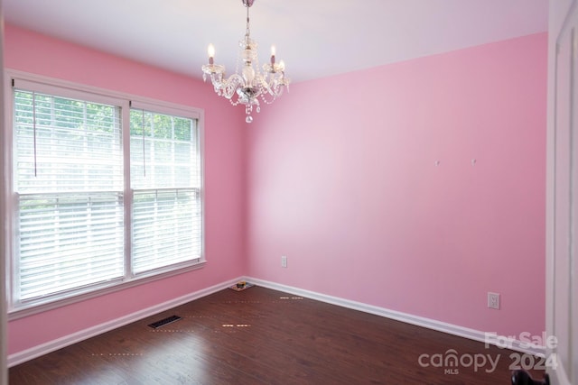 unfurnished room featuring dark wood-type flooring and an inviting chandelier