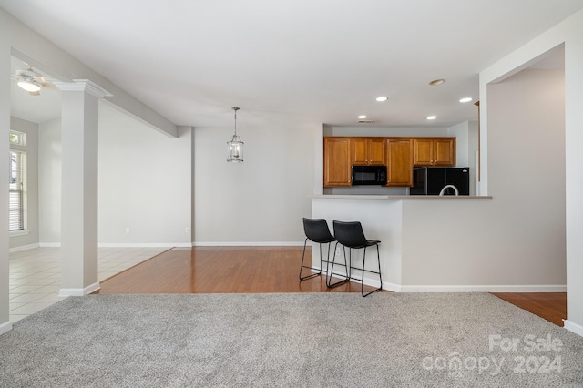 kitchen with light hardwood / wood-style flooring, a kitchen breakfast bar, black appliances, kitchen peninsula, and ceiling fan