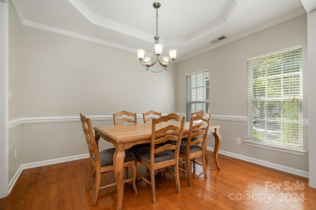 dining area with a tray ceiling, hardwood / wood-style flooring, plenty of natural light, and a notable chandelier