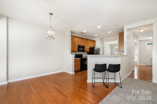 kitchen featuring light wood-type flooring, a chandelier, black appliances, kitchen peninsula, and a breakfast bar