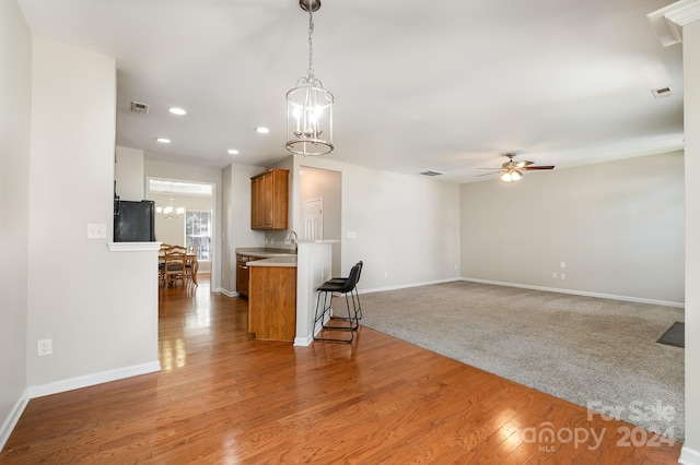 kitchen featuring ceiling fan with notable chandelier, pendant lighting, kitchen peninsula, light colored carpet, and black fridge