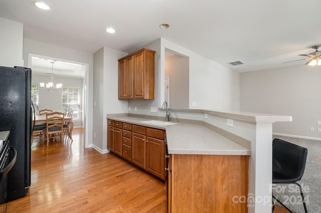 kitchen with ceiling fan with notable chandelier, kitchen peninsula, sink, and light hardwood / wood-style floors