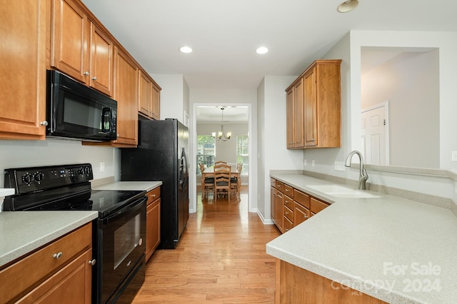 kitchen featuring an inviting chandelier, light hardwood / wood-style flooring, decorative light fixtures, sink, and black appliances