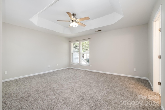 spare room with a tray ceiling, light colored carpet, and ceiling fan