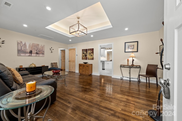 living room featuring dark hardwood / wood-style flooring, a raised ceiling, and an inviting chandelier