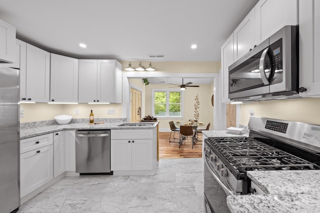 kitchen with ceiling fan, appliances with stainless steel finishes, light stone countertops, white cabinets, and sink