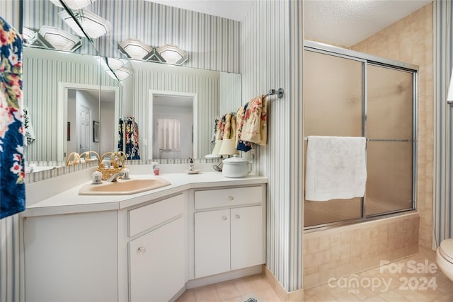 bathroom featuring toilet, a textured ceiling, vanity, tile patterned flooring, and a shower with shower door