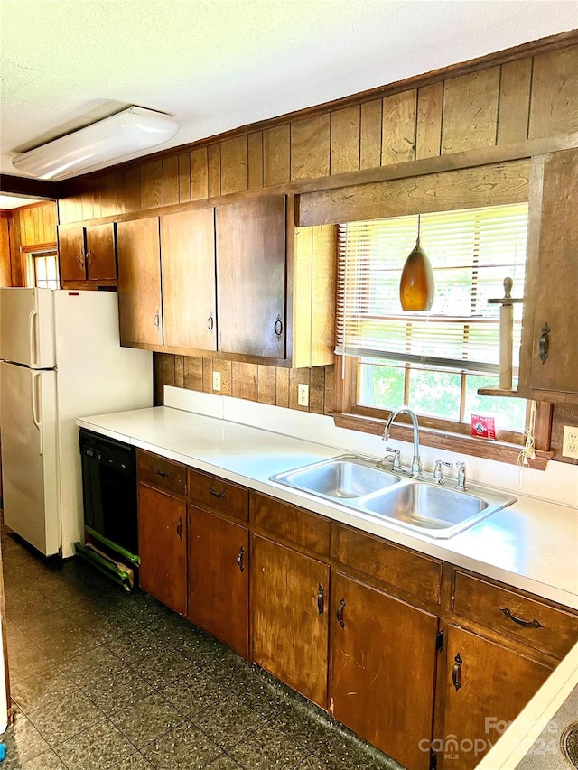 kitchen featuring wood walls, black dishwasher, a textured ceiling, white refrigerator, and sink