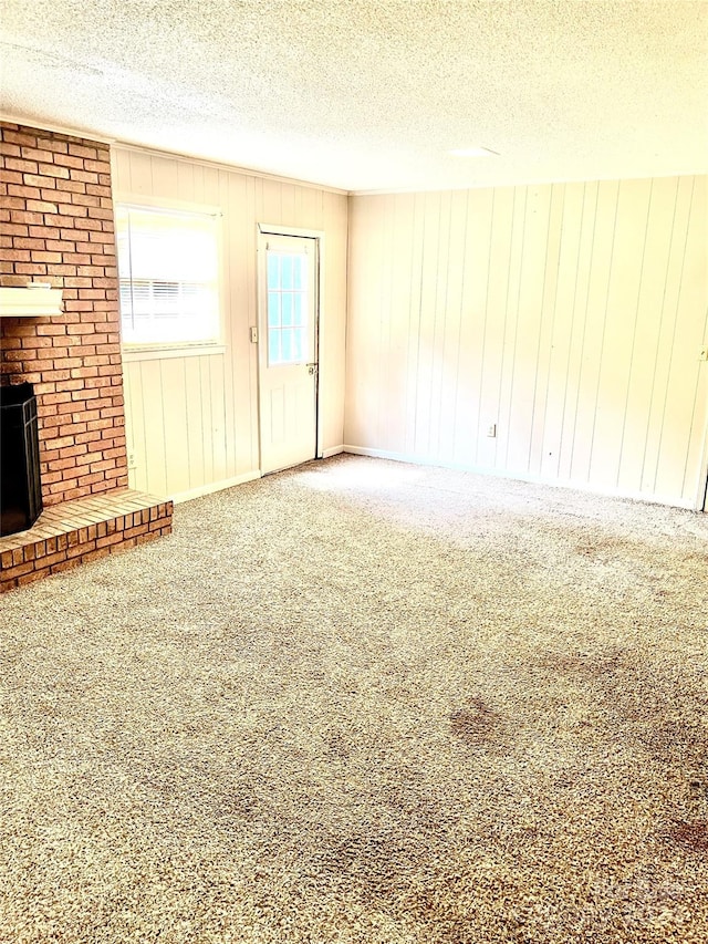 unfurnished living room featuring a brick fireplace, wood walls, a textured ceiling, and carpet flooring