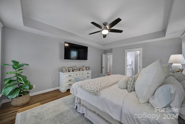 bedroom with hardwood / wood-style floors, ensuite bathroom, ceiling fan, and a raised ceiling