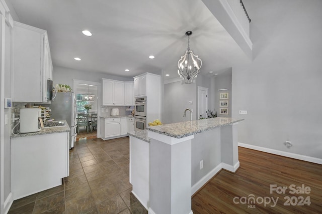 kitchen featuring white cabinetry, light stone countertops, backsplash, pendant lighting, and appliances with stainless steel finishes