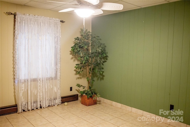 tiled spare room featuring ceiling fan and wood walls
