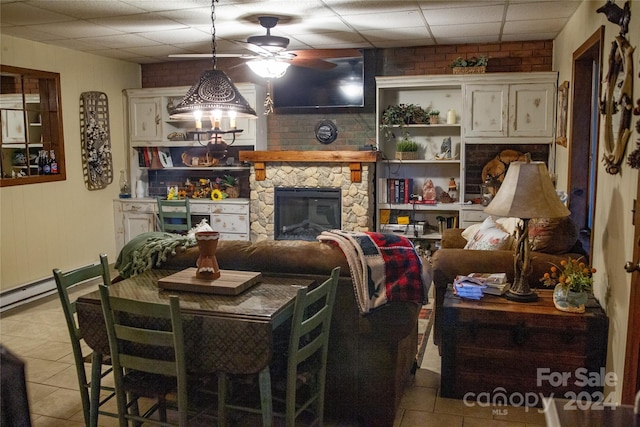 tiled living room featuring a drop ceiling and a stone fireplace