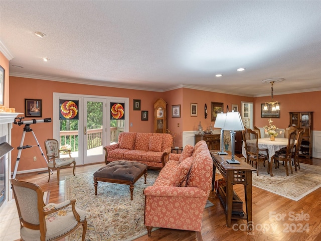 living room featuring light hardwood / wood-style floors, ornamental molding, a textured ceiling, and an inviting chandelier