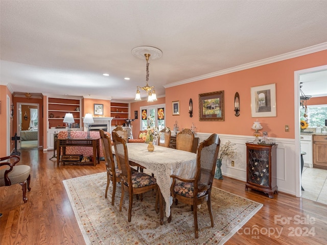 dining area with built in shelves, crown molding, light hardwood / wood-style flooring, and an inviting chandelier