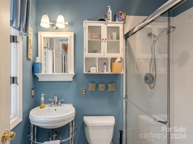 bathroom with toilet, a shower with door, and sink