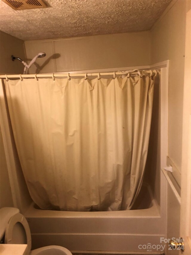 bathroom featuring shower / bath combo with shower curtain, toilet, and a textured ceiling