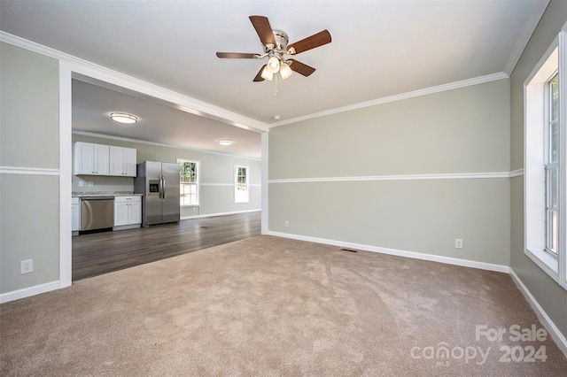 unfurnished living room with dark colored carpet, crown molding, and ceiling fan