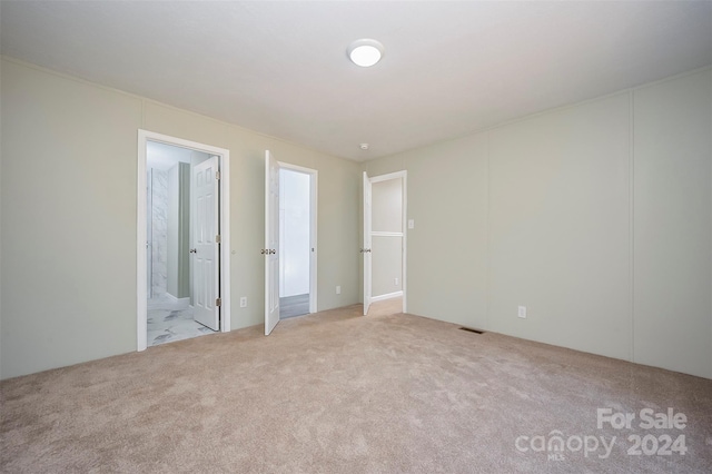 unfurnished bedroom with light carpet and connected bathroom