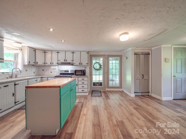 kitchen featuring wood counters, a textured ceiling, stainless steel stove, light hardwood / wood-style flooring, and a center island